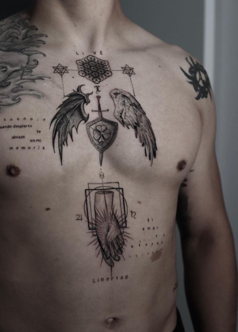 Pecho tatuado: un ala de murciélago a la izquierda y un ala de ave a la derecha, flanqueando una espada clavada en un escudo con un trébol, bajo una flor de la vida entre dos estrellas de seis puntas.