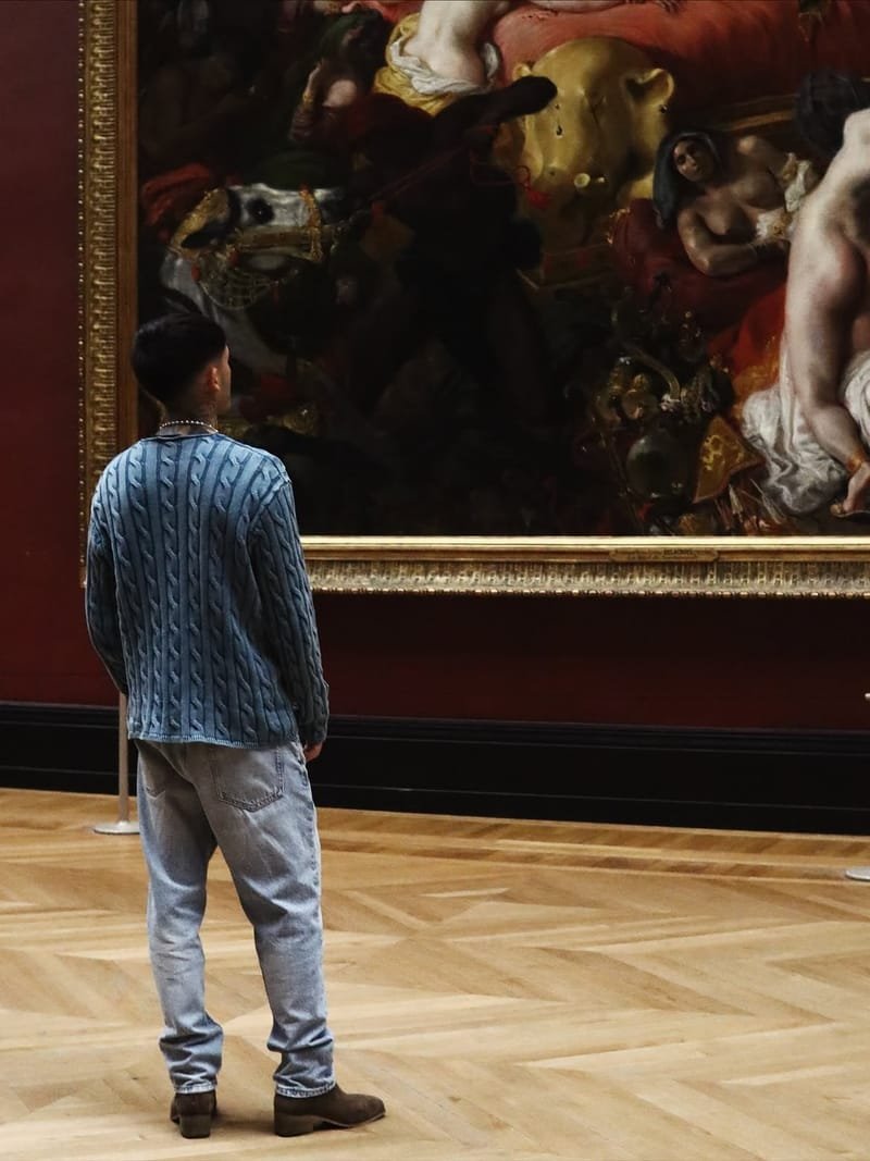 Tomás, de espaldas, ante La muerte de Sardanápalo de Delacroix, en una sala de muros rojos y suelo de parqué.